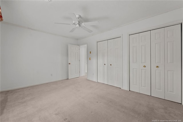 unfurnished bedroom featuring ceiling fan, light carpet, and multiple closets