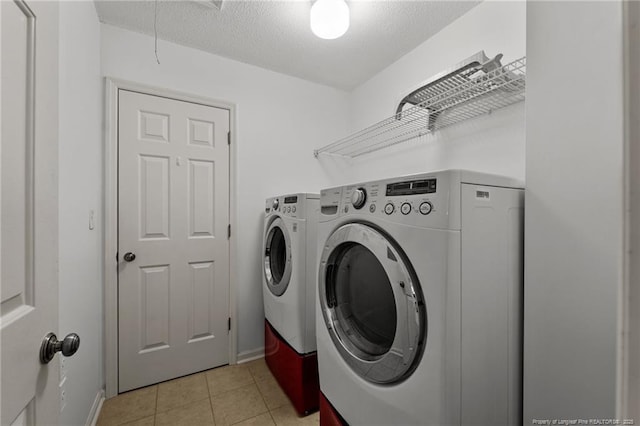 clothes washing area featuring a textured ceiling, washing machine and dryer, and light tile patterned flooring