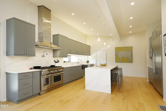 kitchen with gray cabinetry, a sink, appliances with stainless steel finishes, wall chimney exhaust hood, and light countertops