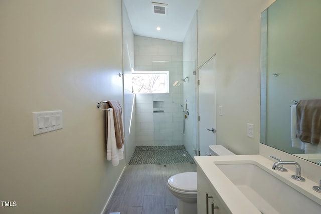 bathroom featuring a tile shower, visible vents, toilet, and vanity