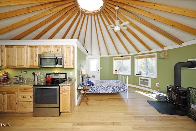 bedroom with light wood finished floors, a wall mounted AC, beam ceiling, a wood stove, and a sink