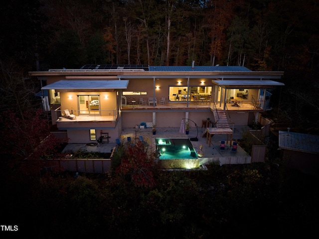 back of house at night with a patio and an outdoor pool