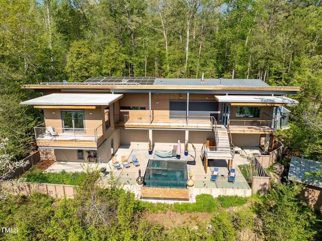 back of house featuring a balcony, a fenced in pool, a patio, and solar panels