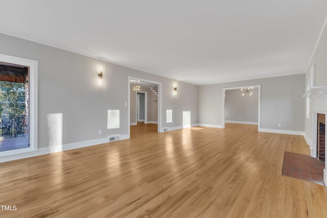 unfurnished living room with a brick fireplace, light hardwood / wood-style flooring, and an inviting chandelier