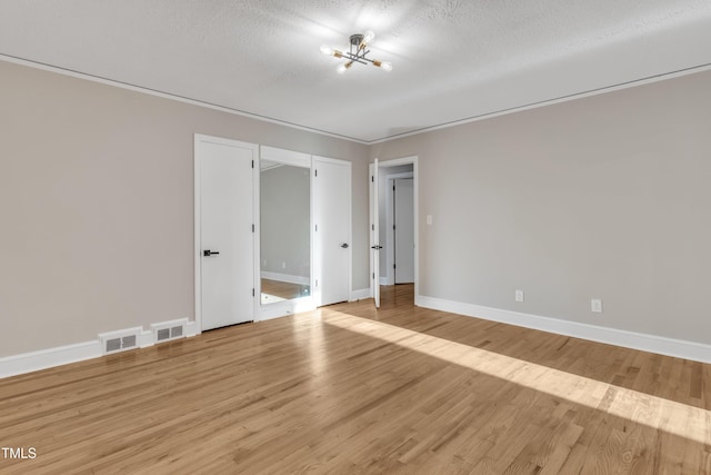 spare room featuring a textured ceiling, an inviting chandelier, and light hardwood / wood-style flooring