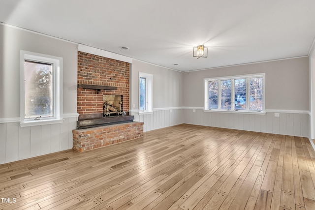 unfurnished living room featuring a fireplace, a wealth of natural light, ornamental molding, and light hardwood / wood-style flooring