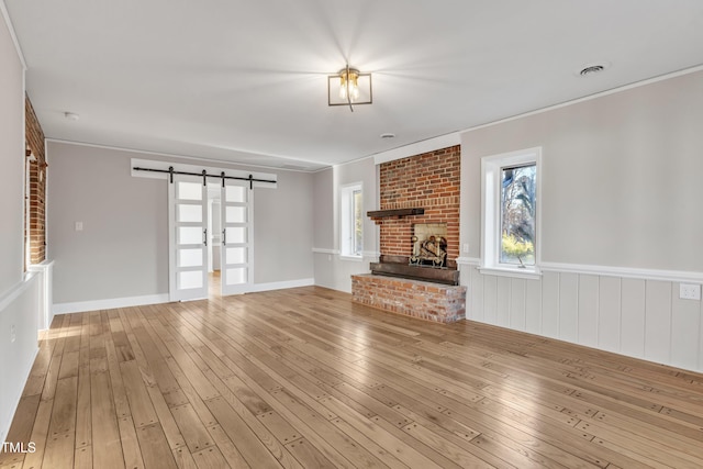 unfurnished living room with a brick fireplace, crown molding, a barn door, and light hardwood / wood-style flooring