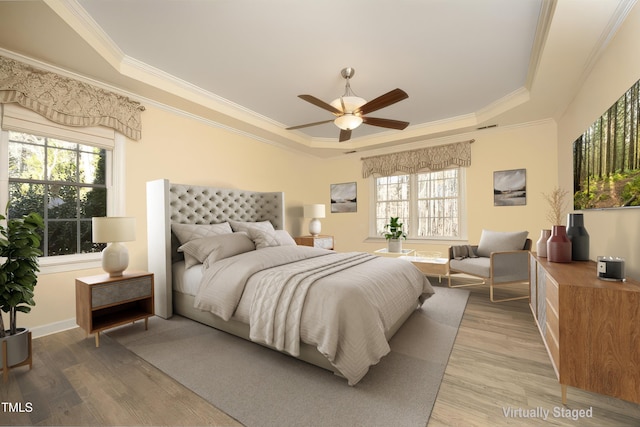 bedroom with ceiling fan, a raised ceiling, light wood-type flooring, and crown molding