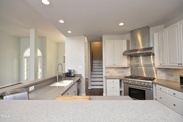 kitchen with tasteful backsplash, stainless steel appliances, sink, wall chimney range hood, and white cabinetry