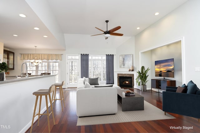 living room featuring sink, high vaulted ceiling, dark wood-type flooring, and ceiling fan with notable chandelier