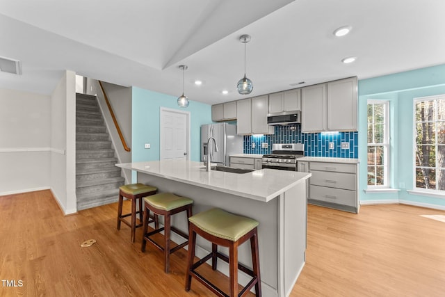 kitchen featuring decorative backsplash, lofted ceiling, gray cabinets, a kitchen island with sink, and appliances with stainless steel finishes