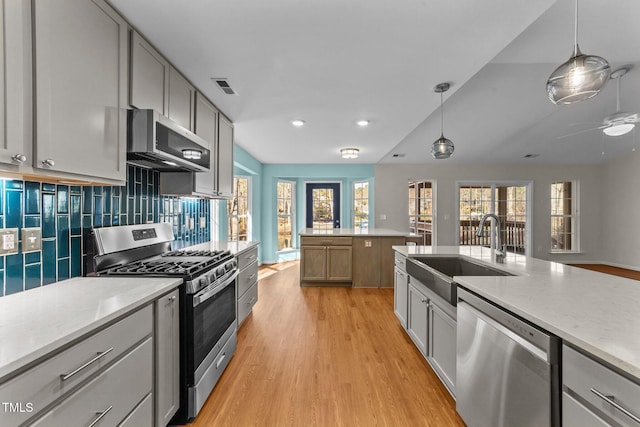 kitchen with sink, hanging light fixtures, light wood-type flooring, appliances with stainless steel finishes, and tasteful backsplash