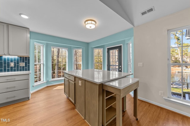 kitchen featuring gray cabinetry, a center island, lofted ceiling, decorative backsplash, and light wood-type flooring