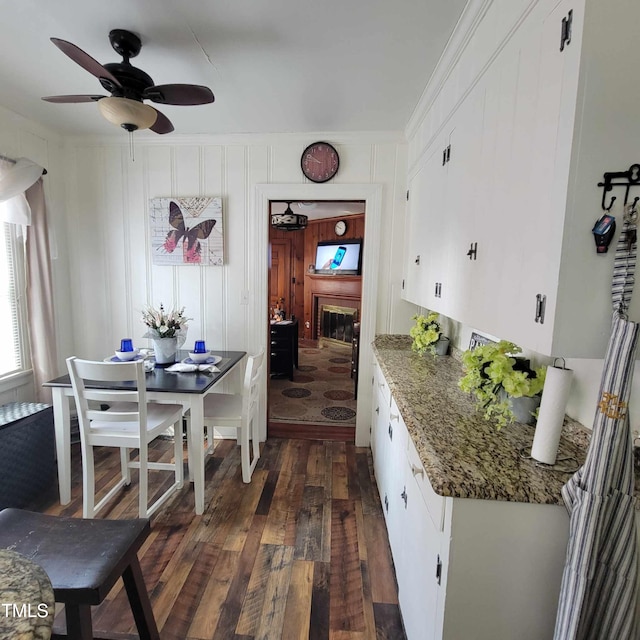 dining space featuring ceiling fan, dark wood-type flooring, and a glass covered fireplace