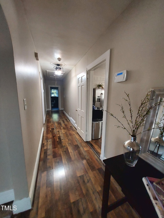 hall with dark wood-type flooring, arched walkways, attic access, and baseboards