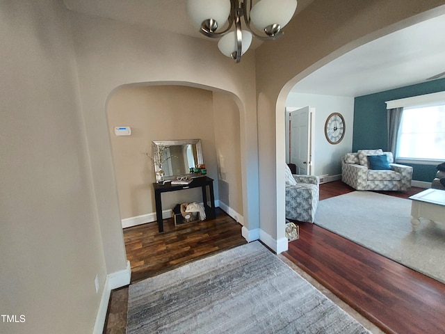 hallway with a notable chandelier, baseboards, arched walkways, and wood finished floors