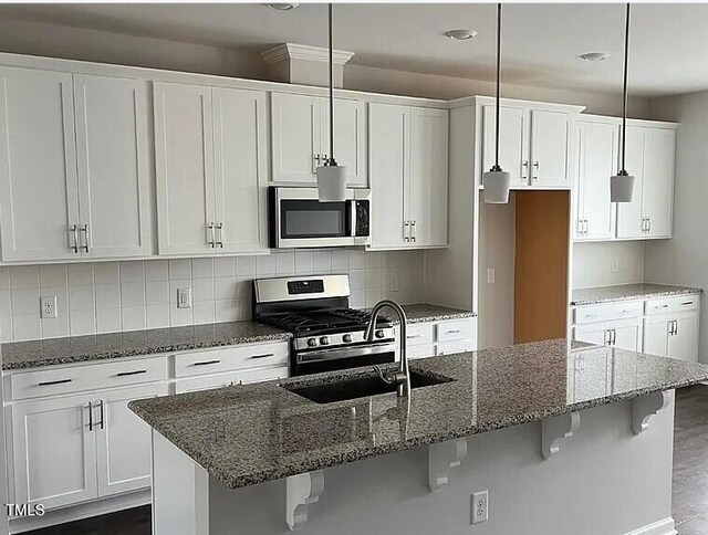 1009 Manorhaven Dr, Durham, NC 27703 - kitchen with appliances with stainless steel finishes, a kitchen breakfast bar, white cabinetry, tasteful backsplash, and an island with sink