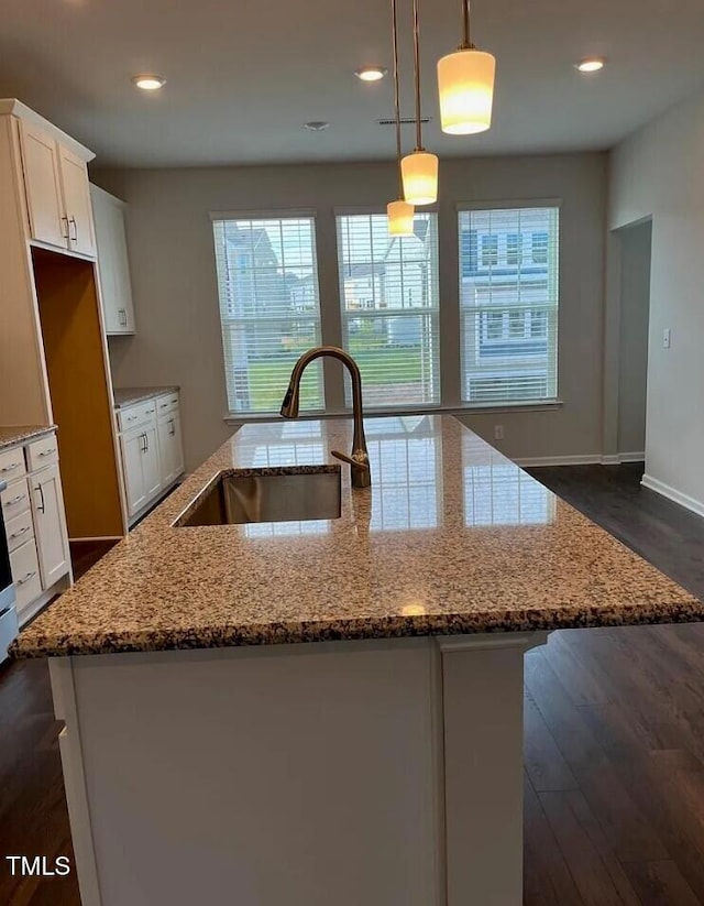 1009 Manorhaven Dr, Durham, NC 27703 - kitchen with an island with sink, dark wood-style floors, light stone countertops, white cabinets, and hanging light fixtures