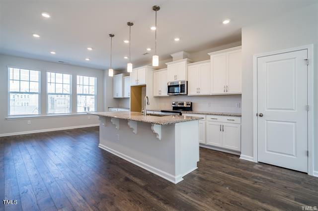 1009 Manorhaven Dr, Durham, NC 27703 - kitchen featuring appliances with stainless steel finishes, white cabinets, dark wood-style flooring, light stone counters, and a breakfast bar area