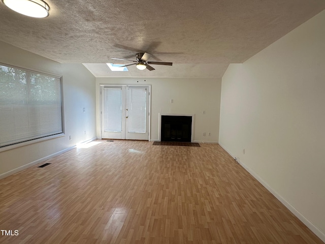 unfurnished living room featuring light wood-type flooring, a wealth of natural light, a textured ceiling, vaulted ceiling, and ceiling fan