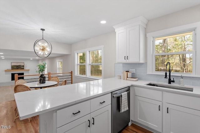 kitchen with sink, white cabinetry, hanging light fixtures, stainless steel dishwasher, and kitchen peninsula