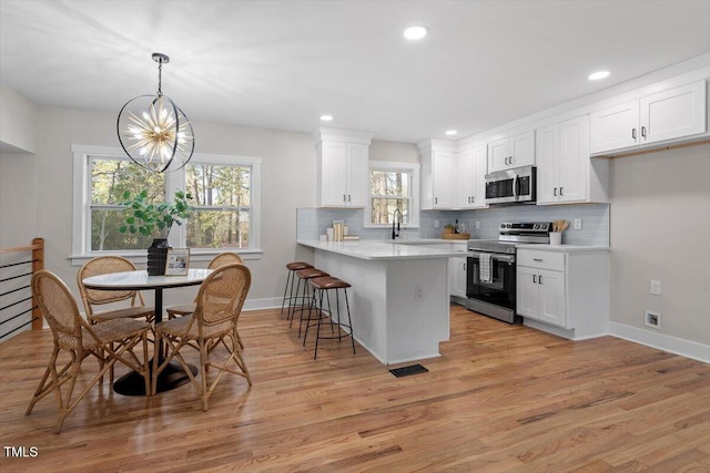 kitchen with a breakfast bar area, white cabinetry, hanging light fixtures, kitchen peninsula, and stainless steel appliances