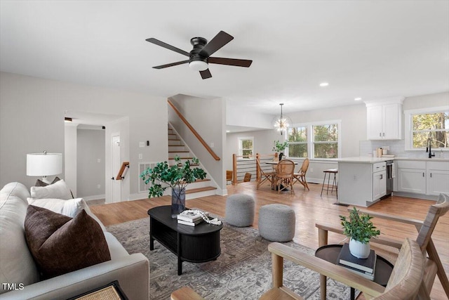 living room featuring ceiling fan with notable chandelier, sink, and light wood-type flooring