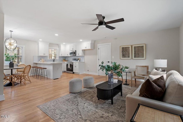 living room featuring ceiling fan with notable chandelier, sink, and light hardwood / wood-style floors