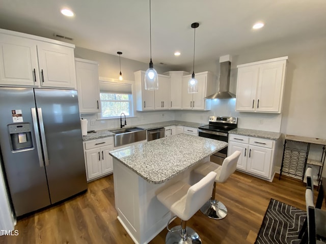 kitchen with stainless steel appliances, wall chimney range hood, a kitchen island, decorative light fixtures, and white cabinets