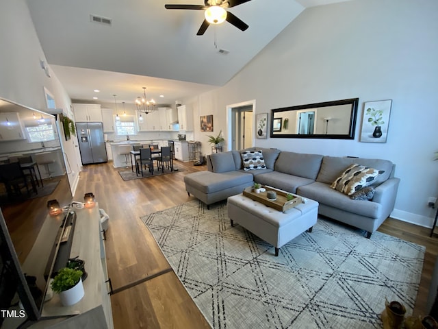 living room with hardwood / wood-style floors, high vaulted ceiling, and ceiling fan with notable chandelier