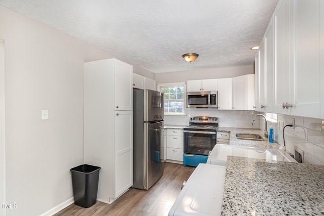 kitchen with white cabinets, appliances with stainless steel finishes, light stone counters, and sink