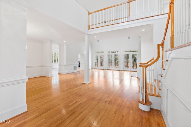 unfurnished living room featuring a high ceiling, light hardwood / wood-style floors, ornate columns, and french doors