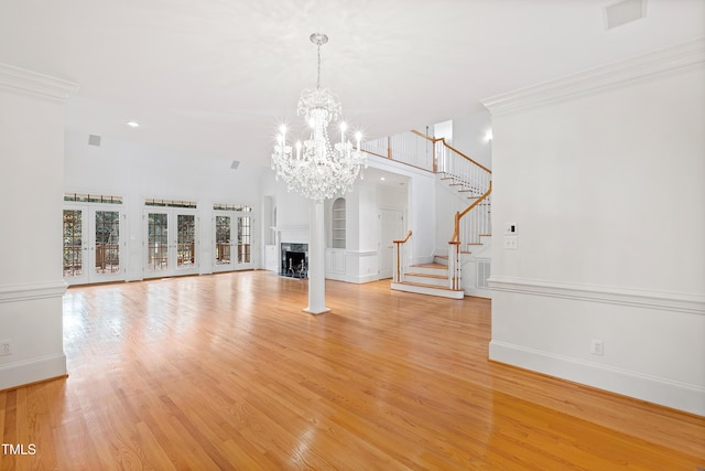 unfurnished living room with a towering ceiling, ornamental molding, an inviting chandelier, light hardwood / wood-style flooring, and a fireplace