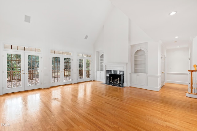 unfurnished living room featuring french doors, built in features, a high end fireplace, high vaulted ceiling, and light wood-type flooring