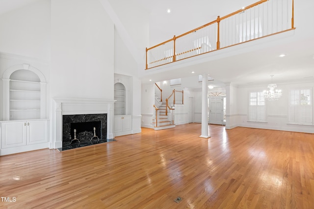 unfurnished living room featuring a high ceiling, built in shelves, a premium fireplace, ornate columns, and light hardwood / wood-style floors