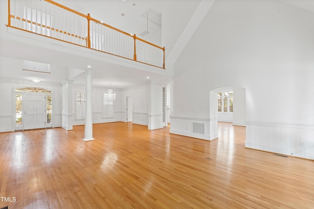 unfurnished living room featuring a high ceiling, decorative columns, light hardwood / wood-style flooring, and a wall unit AC