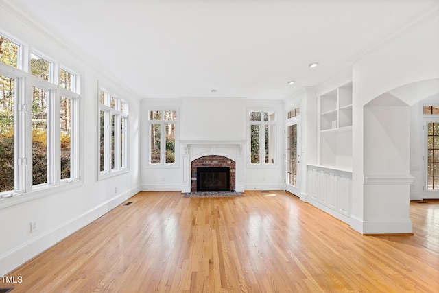 unfurnished living room with built in shelves, light hardwood / wood-style floors, a brick fireplace, and ornamental molding