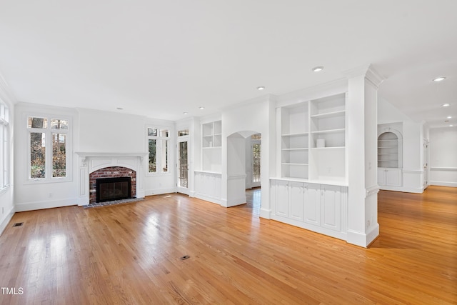 unfurnished living room featuring a wealth of natural light, built in features, ornamental molding, and a brick fireplace