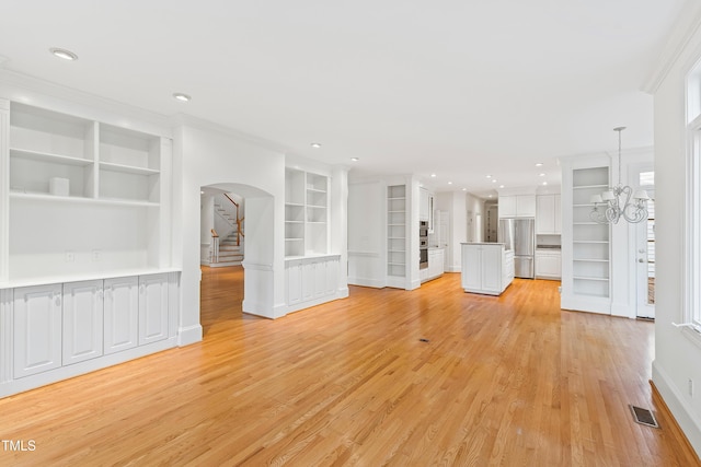 unfurnished living room featuring built in shelves, crown molding, light wood-type flooring, and an inviting chandelier