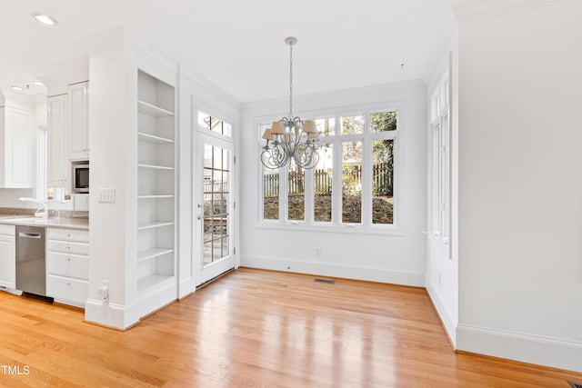 unfurnished dining area featuring crown molding, built in features, light hardwood / wood-style floors, and an inviting chandelier