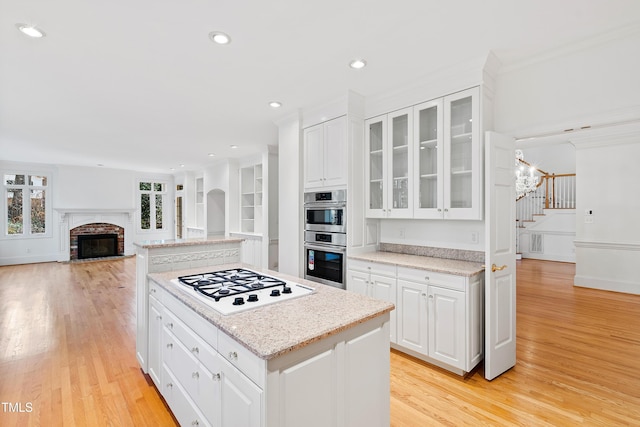 kitchen with white cabinets, a kitchen island, stainless steel double oven, and white gas cooktop