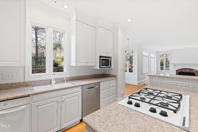 kitchen with sink, white cabinetry, stainless steel appliances, and a brick fireplace