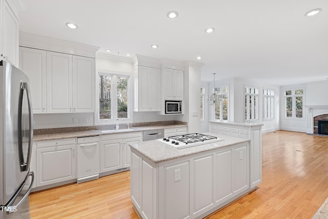 kitchen with a brick fireplace, white cabinetry, pendant lighting, and appliances with stainless steel finishes