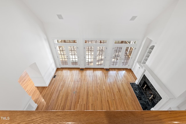 unfurnished living room featuring a fireplace, french doors, a towering ceiling, and hardwood / wood-style floors