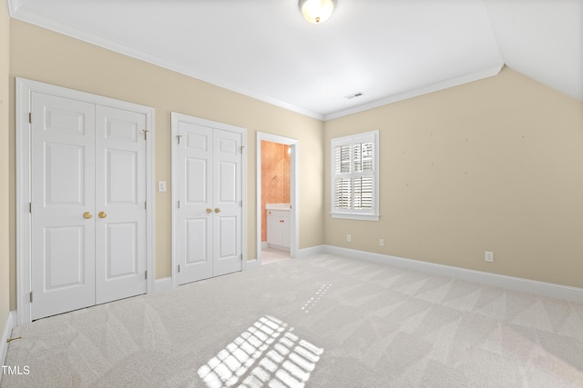 unfurnished bedroom featuring ensuite bath, crown molding, light colored carpet, and two closets