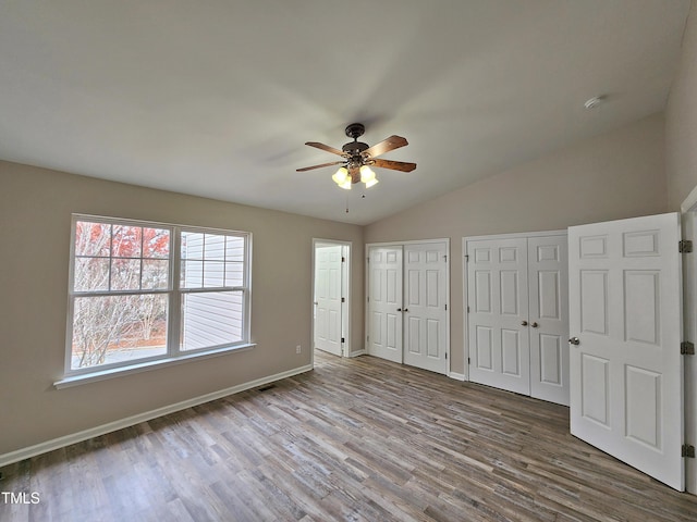 unfurnished bedroom with multiple closets, ceiling fan, vaulted ceiling, and hardwood / wood-style flooring