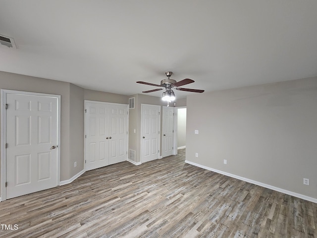 unfurnished bedroom with multiple closets, ceiling fan, and light wood-type flooring