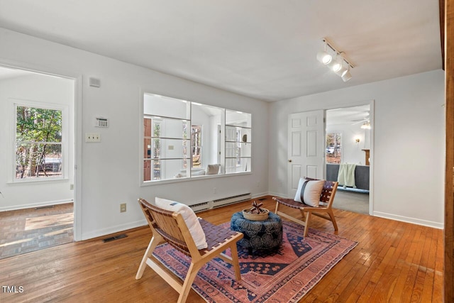 living area featuring a baseboard heating unit, hardwood / wood-style flooring, baseboards, and visible vents