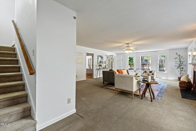 carpeted living area with baseboards, stairway, a textured ceiling, and ceiling fan