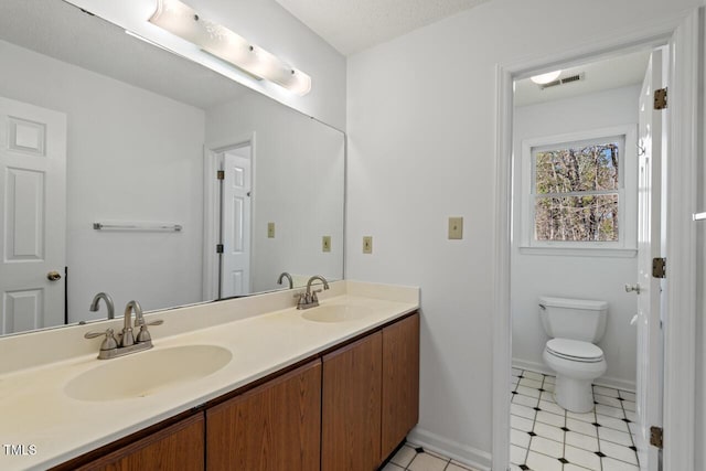 full bathroom with double vanity, toilet, visible vents, and a sink